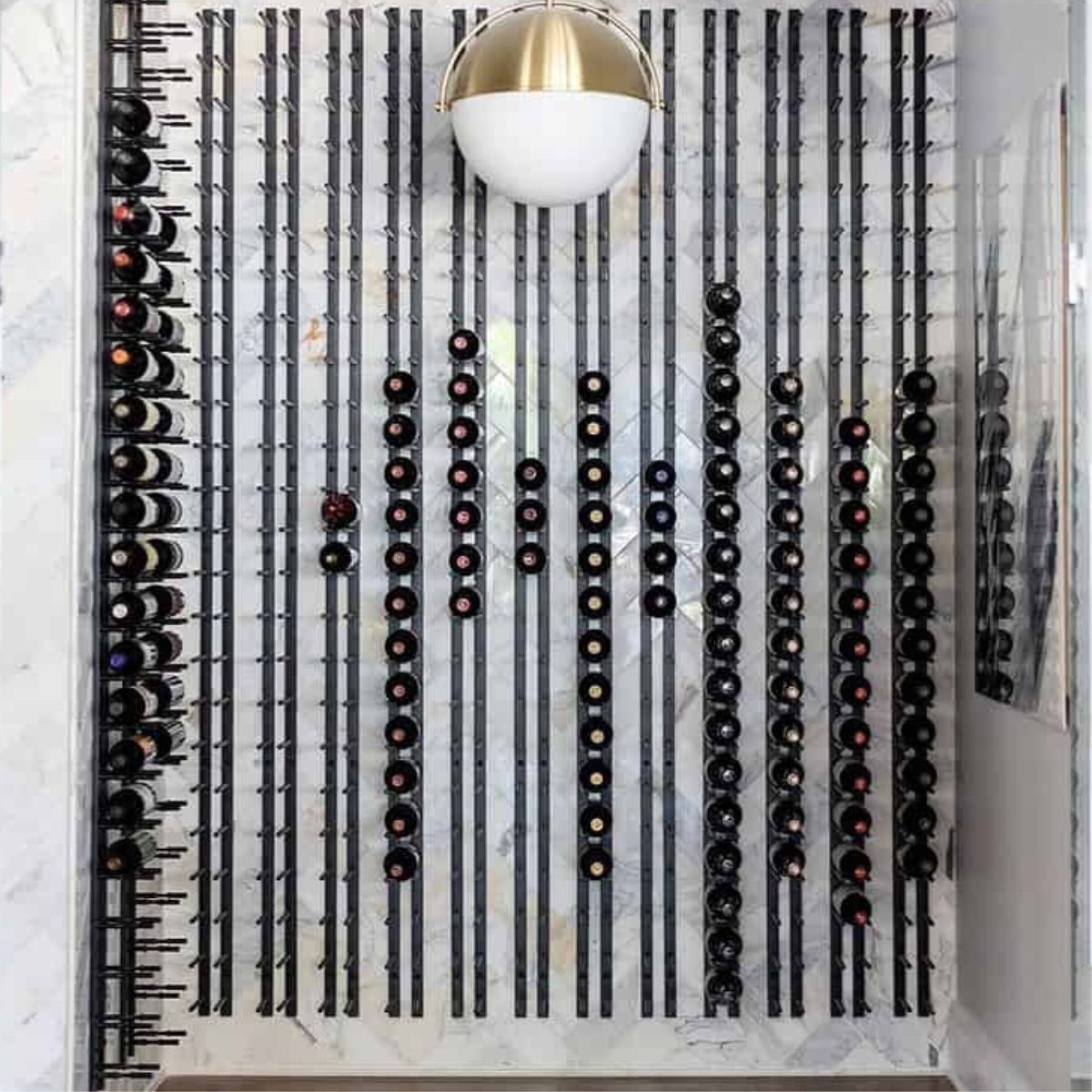 Ultra 4FT Cork-Out Straight Wall Rail Wine Rack (12 Bottles) - Floor-to-ceiling wine wall with black metal racks against a marble backdrop and modern light fixture