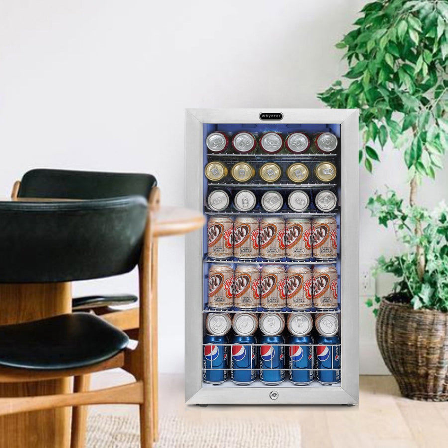 Whynter BR-128WS 17" Freestanding Beverage Refrigerator - filled with soda cans beside a dining table and indoor plant