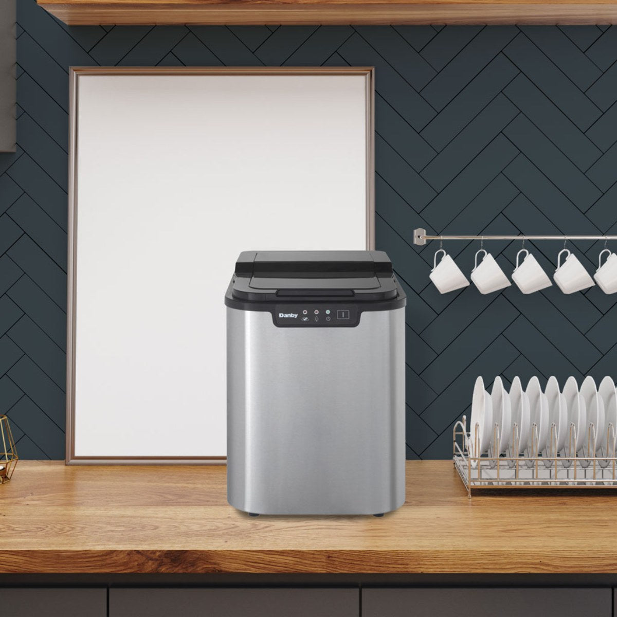 Danby 25 lbs. Countertop Ice Maker in Stainless Steel - placed on a wooden counter with navy backsplash and white mugs