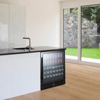 NewAir 24” Built-In 177-Can Beverage Fridge in Black Stainless Steel - Black beverage fridge filled with drinks beside a gray sofa in a modern living room