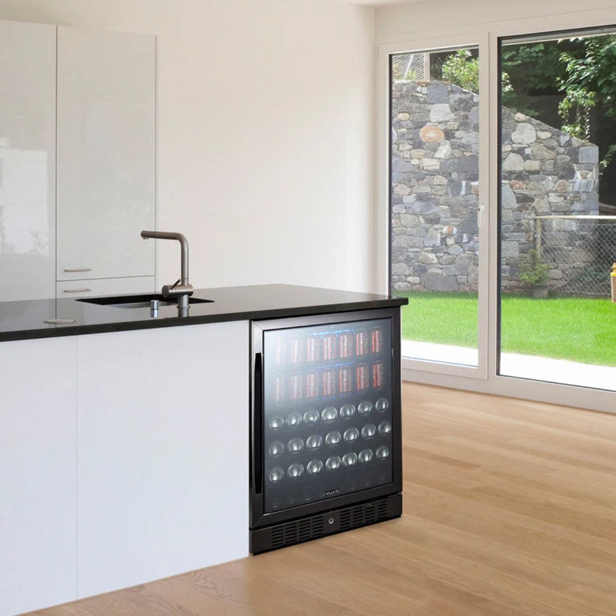 NewAir 24” Built-In 177-Can Beverage Fridge in Black Stainless Steel - Black beverage fridge filled with drinks beside a gray sofa in a modern living room