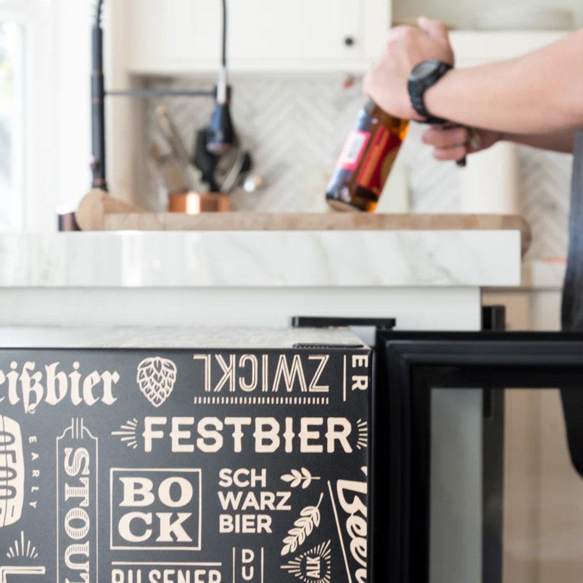 Newair 126-Can Freestanding Beers of the World Fridge with SplitShelf - Person opening a bottle next to a beer-patterned fridge
