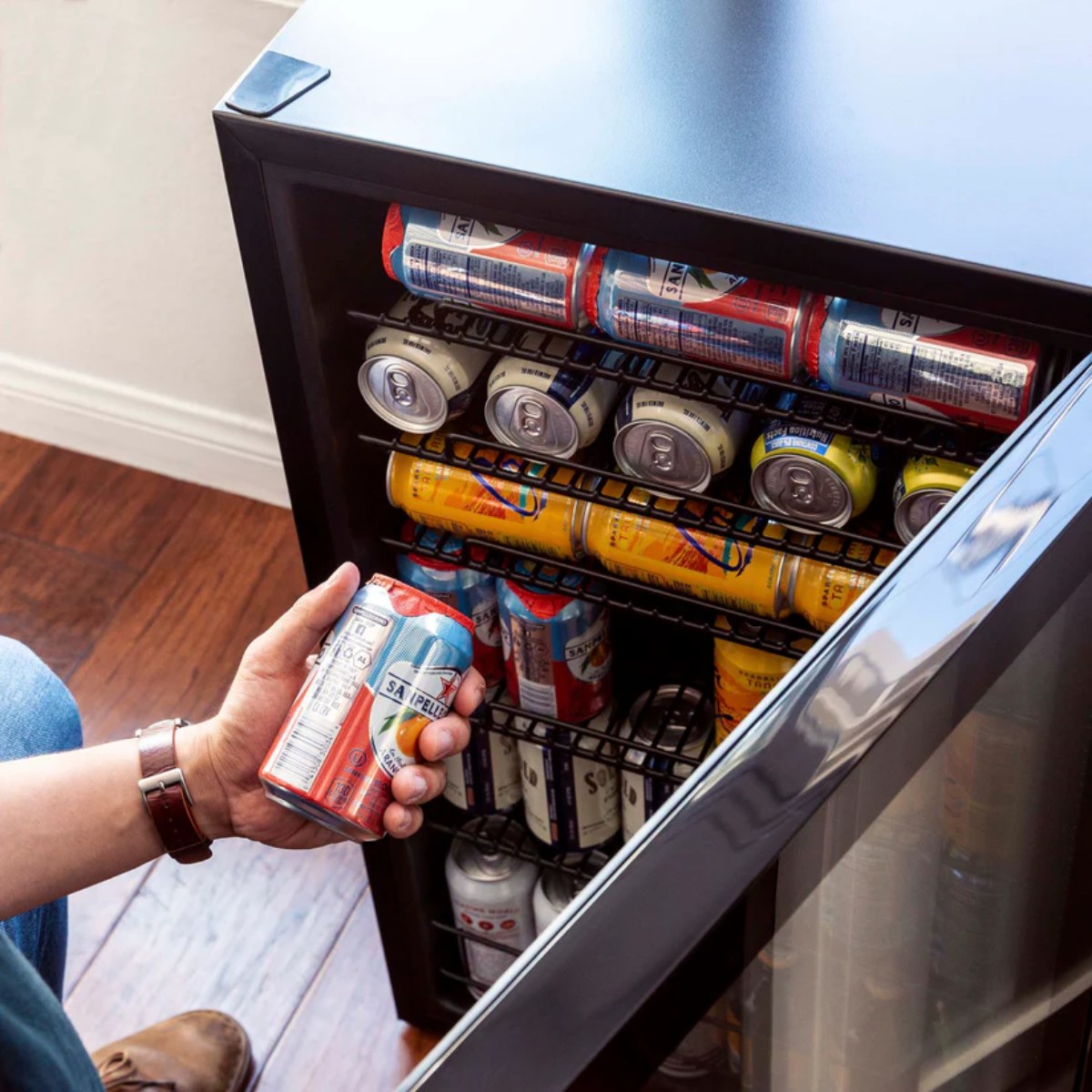 Newair 126-Can Freestanding Beverage Fridge – 19″ Black - Person taking a canned drink from a beverage fridge filled with assorted cans