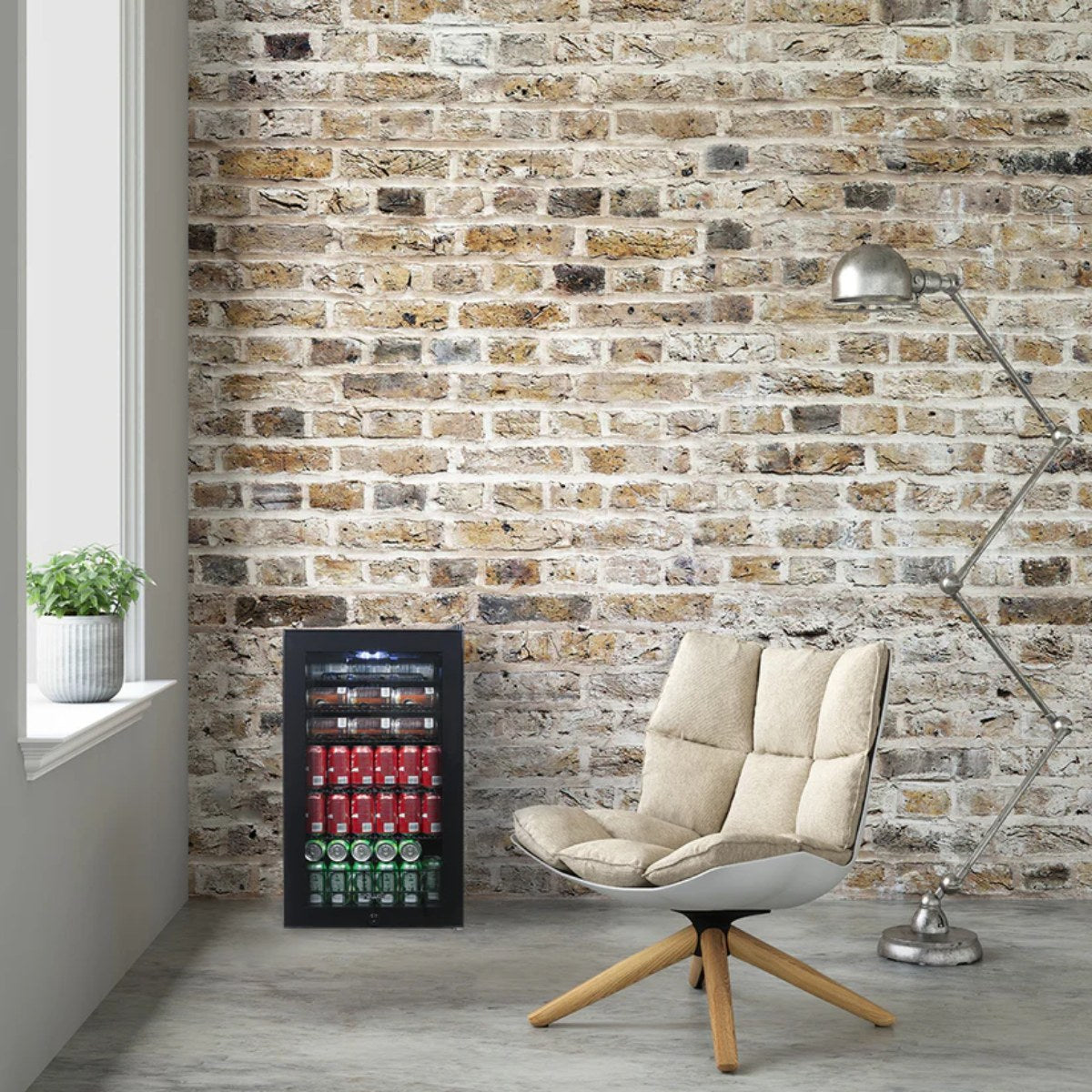 Newair 126-Can Freestanding Beverage Fridge – 19″ Black - fridge against a brick wall beside a modern cushioned chair and floor lamp