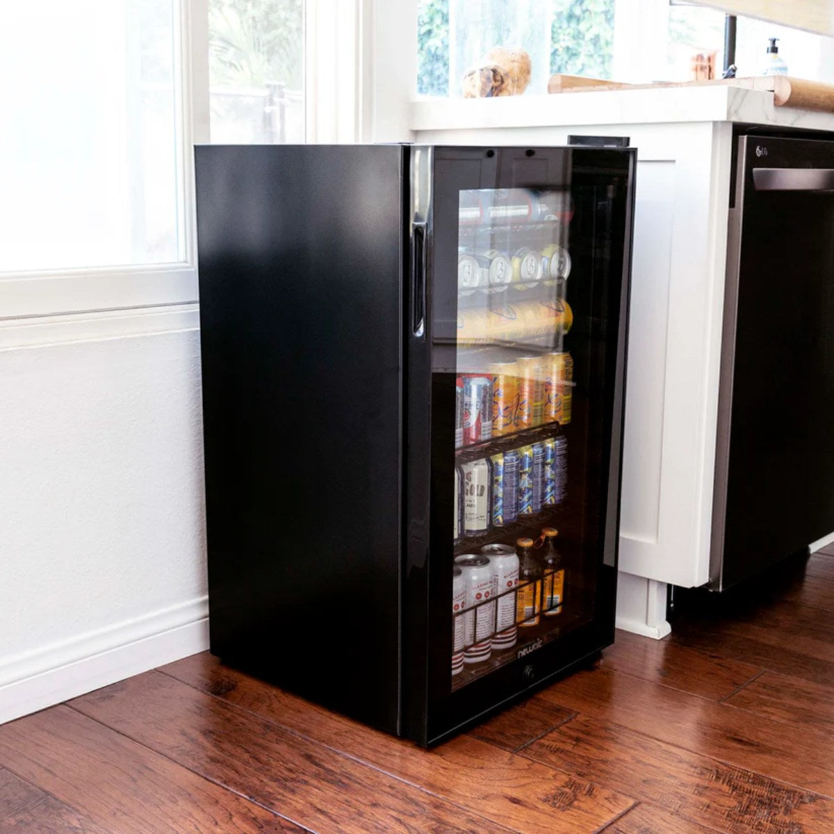 Newair 126-Can Freestanding Beverage Fridge – 19″ Black - fridge positioned beside a kitchen counter near a window on wood flooring