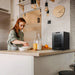 Newair 12 Bottle Shadow-T Series Wine Fridge – 9.9" Black - Compact Fridge shown on top of the table with a woman preparing foods and drinks