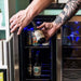 Newair 24” Dual Zone Wine and Beverage Fridge in Stainless Steel - Man grabbing a beer bottle from a beverage and wine fridge