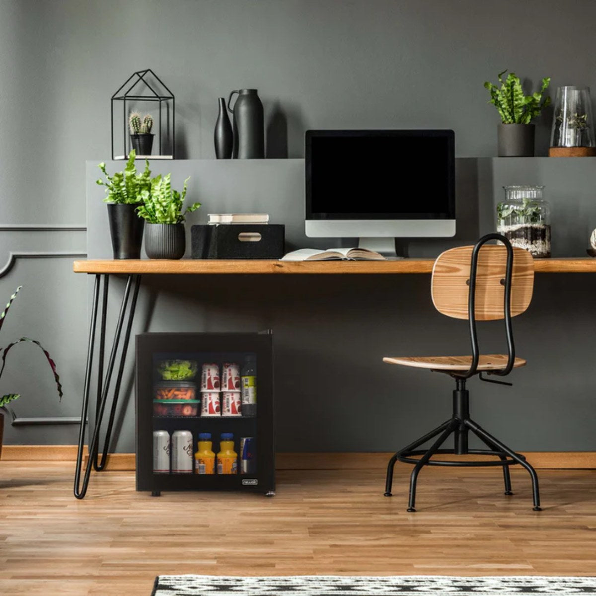 Newair 60-Can Freestanding Beverage Fridge – 16.75" Black - placed under a wooden desk in a modern home office with plants, a computer, and a wooden chair