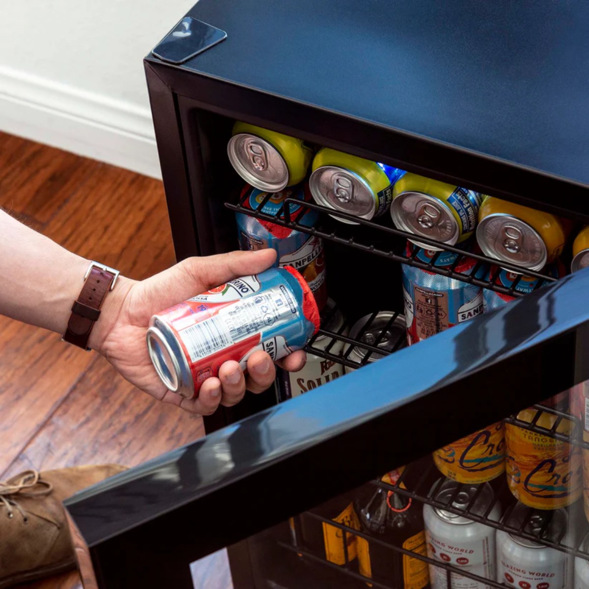 Newair 90-Can Freestanding Beverage Fridge – 17″ Black - Person taking a canned drink from a beverage fridge filled with assorted cans