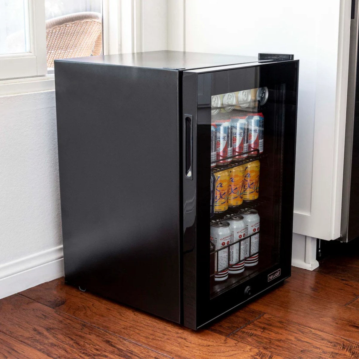 Newair 90-Can Freestanding Beverage Fridge – 17″ Black - fridge filled with canned drinks positioned next to a kitchen