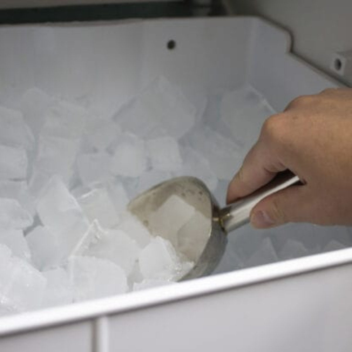 Silhouette 15″ Built-in Under Counter Ice Maker in Stainless Steel - hand using a metal scoop to collect clear ice cubes from an ice maker bin