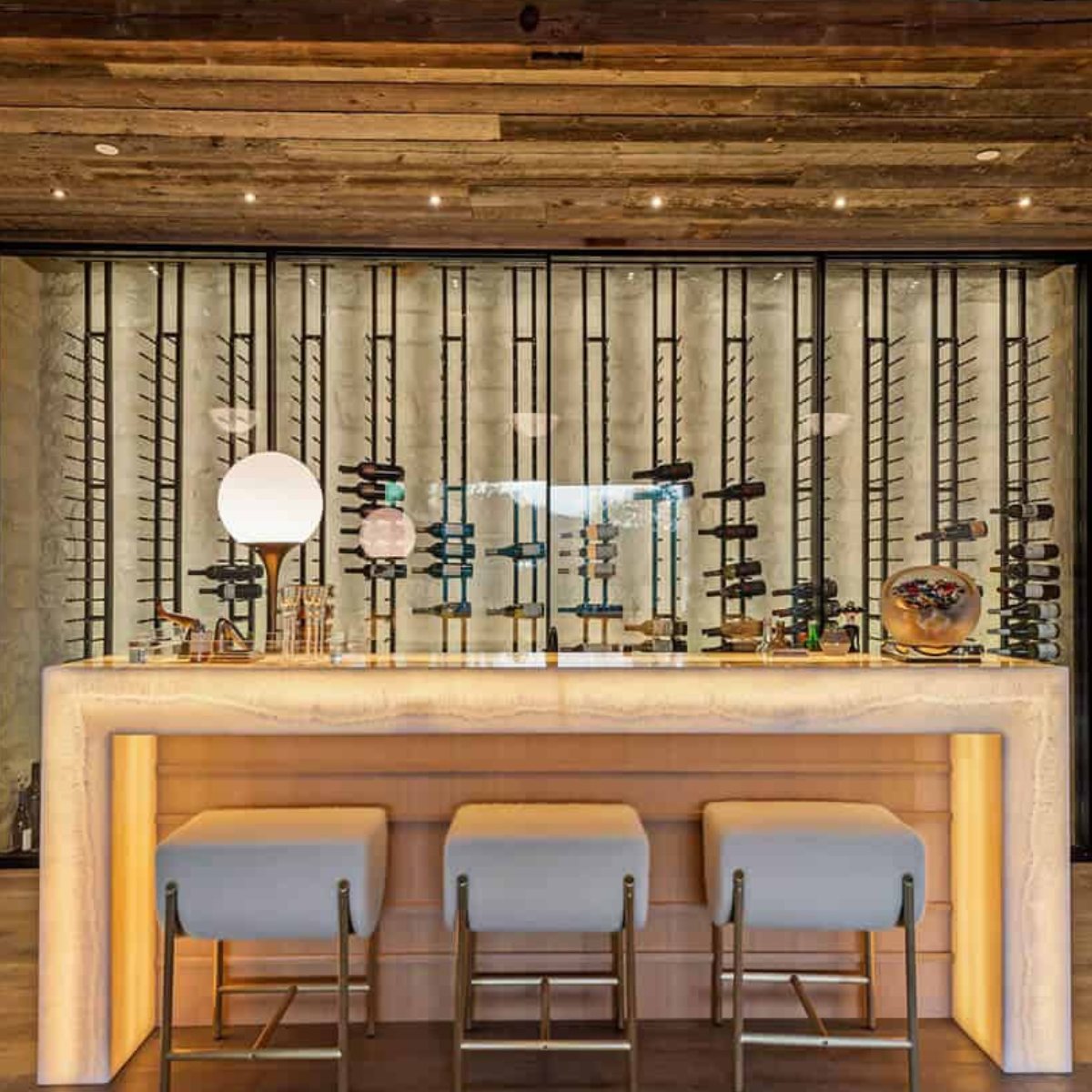 Ultra Floor-to-Ceiling Mounted 1-Sided Wine Rack Display (42 Bottles) - Backlit home bar with three stools and tall vertical wine racks behind glass