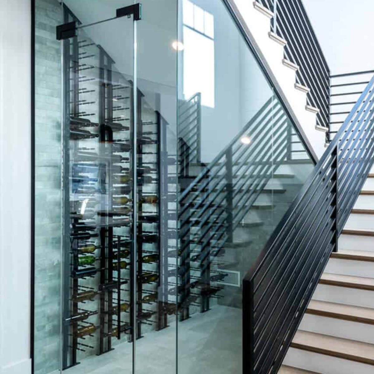 Ultra Floor-to-Ceiling Mounted 1-Sided Wine Rack Display (42 Bottles) - Glass-enclosed wine cellar built under a modern staircase with metal railings