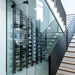 Ultra Floor-to-Ceiling Mounted 1-Sided Wine Rack Display (42 Bottles) - Glass-enclosed wine cellar built under a modern staircase with metal railings