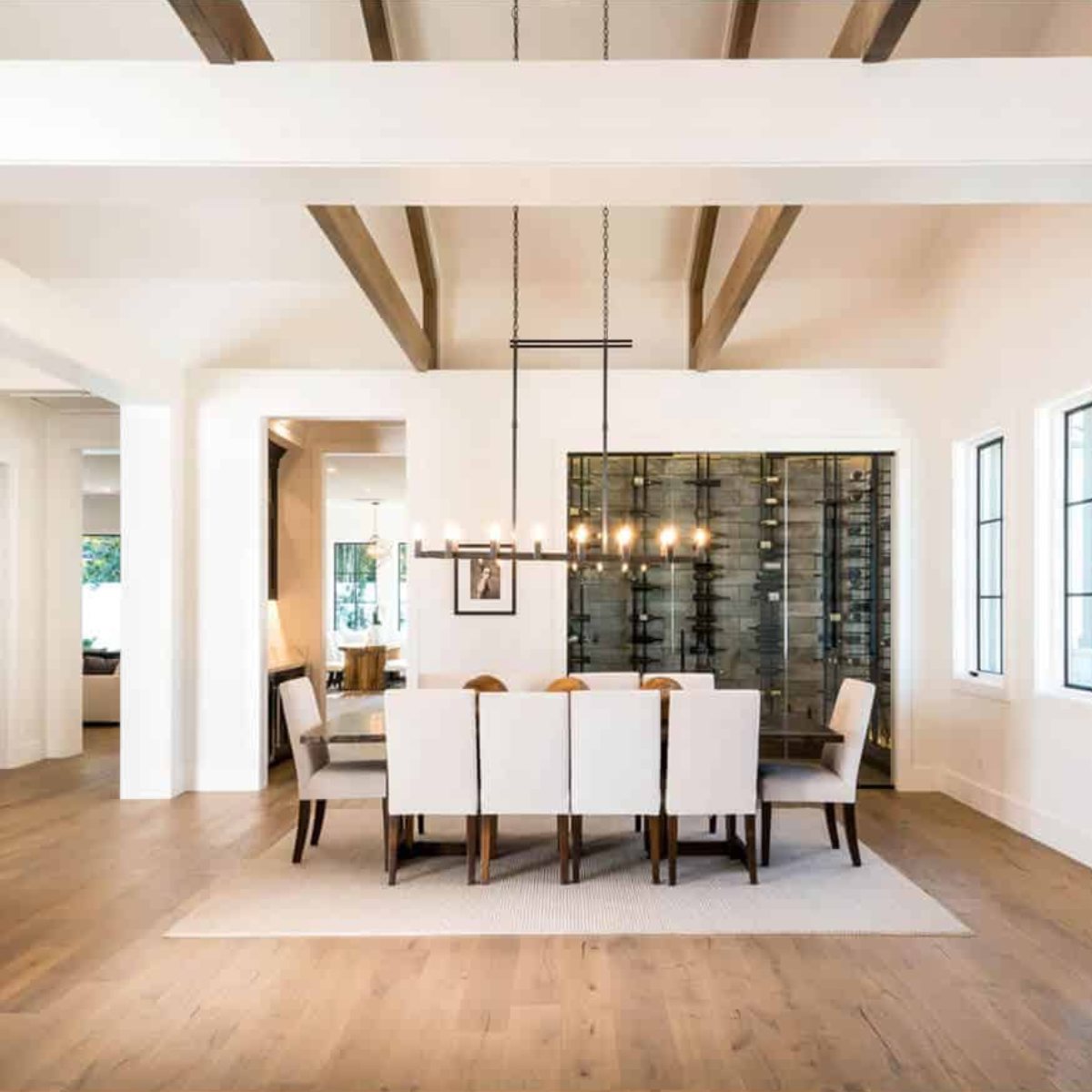 Ultra Floor-to-Ceiling Mounted 1-Sided Wine Rack Display (63 Bottles) - Bright dining room with a long table and chairs facing a glass-enclosed wine wall