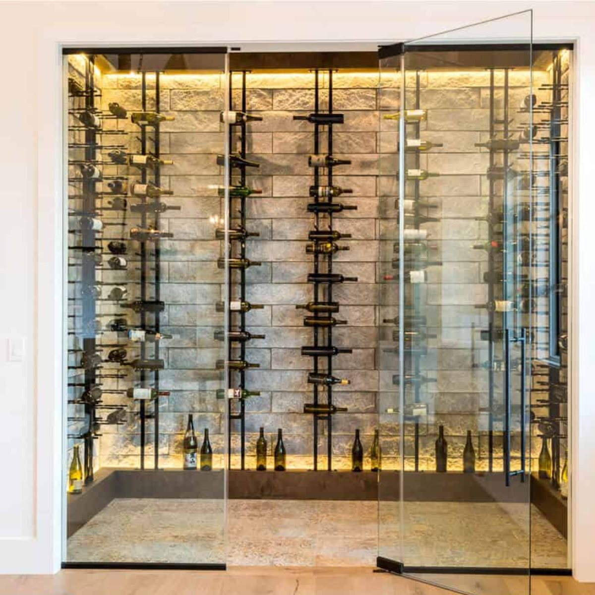 Ultra Floor-to-Ceiling Mounted 1-Sided Wine Rack Display (63 Bottles) - Glass wine cellar with stone wall and backlit racks holding bottles in a modern display