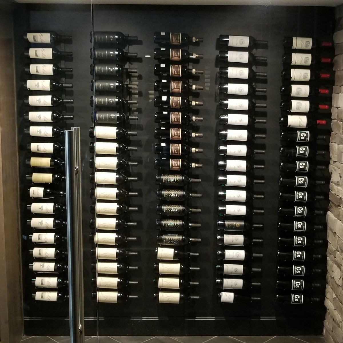 VintageView 2 Foot wall mounted wine storage rack installed behind glass with label forward bottle display in a custom cellar wall