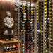 VintageView 6 Foot wall mounted wine storage rack installed on a stone accent wall with label forward bottles and decorative sculpture