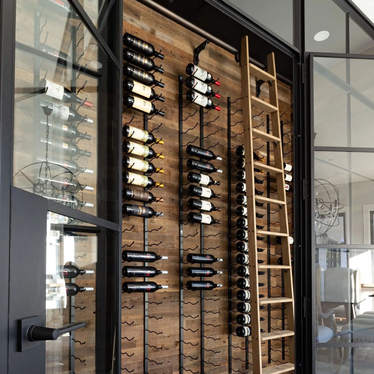 VintageView 8 Foot wall mounted wine storage rack installed on a wood accent wall with rolling ladder inside a glass wine room
