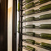 VintageView Perch 1 bottle vertical wall mounted wine rack installed on a modern wall with horizontally stored wine bottles nearby