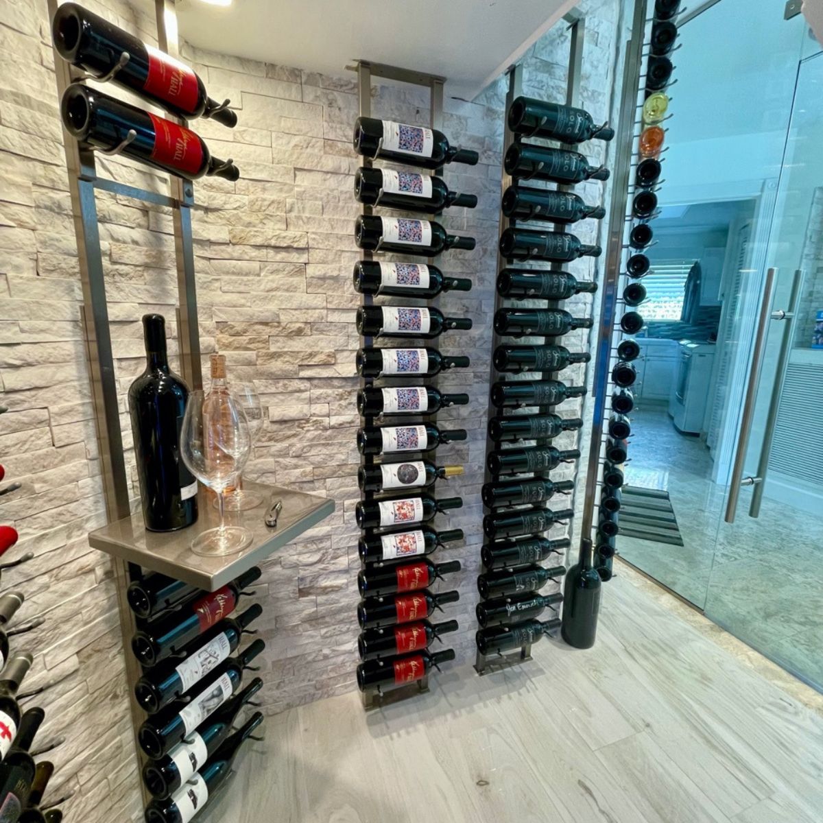 VintageView wall mounted wine cellar shelf installed on a stacked stone wall with vertical wine bottle columns and integrated display shelf