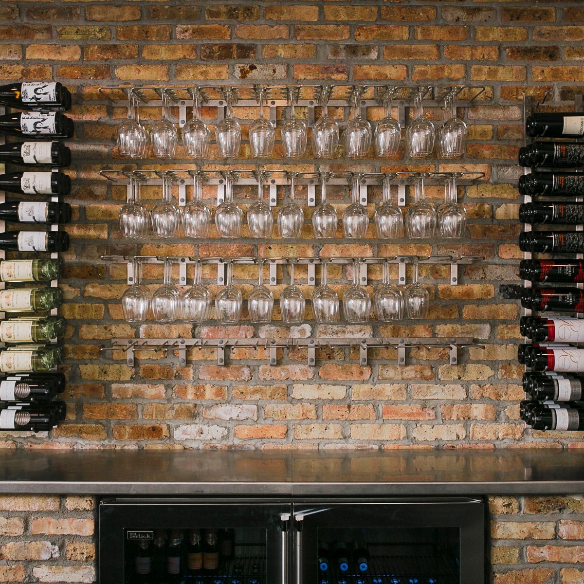 Leading wall mounted wine glass stemware rack installed on a brick wall wine bar with multiple rows of hanging glassware