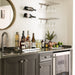 VintageView wall mounted wine glass stemware rack installed above a home bar counter with hanging wine glasses and liquor bottles